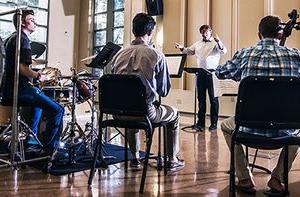 Three students play instruments while a professor conducts